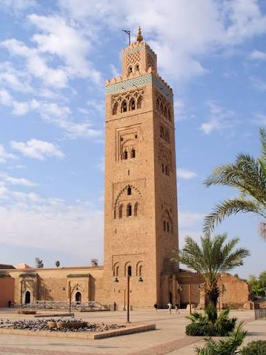 The Koutoubia Mosque minaret rising above the palm trees of Marrakech — the 12th-century Almohad tower that served as the architectural model for the Giralda of Seville and the Hassan Tower of Rabat, and remains the defining vertical element of the Marrakech skyline